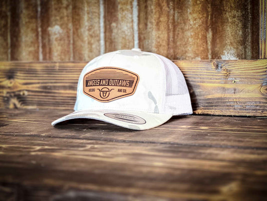 White and grey mesh back trucker hat with a leather patch that has the Angels and Outlaws Co name and log engraved on it