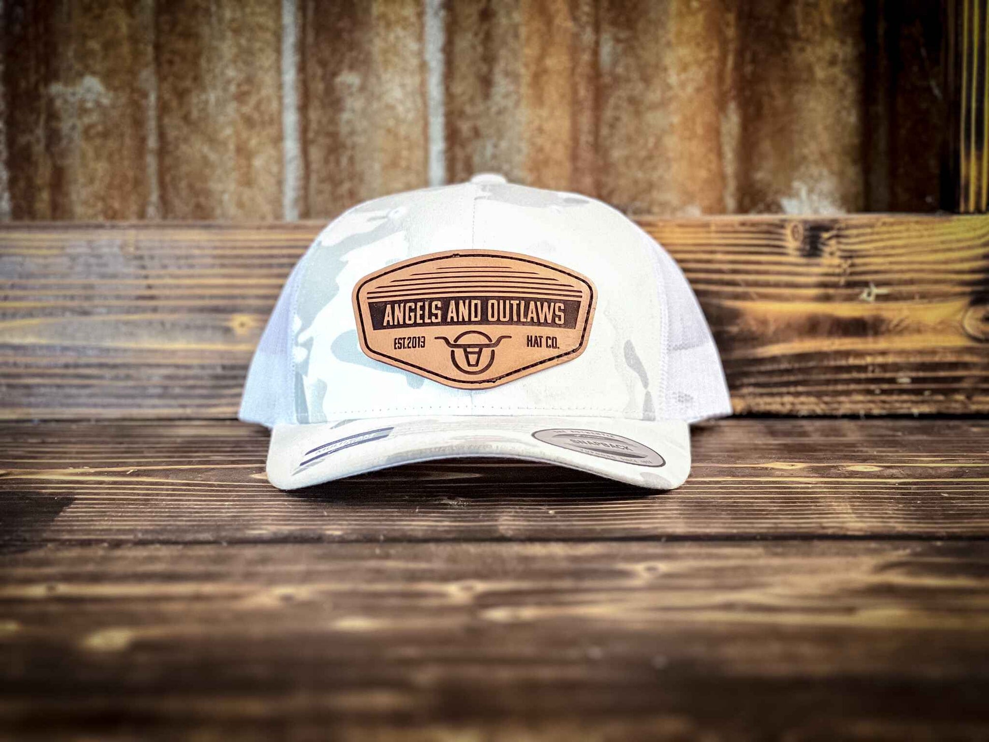 White and grey mesh back trucker hat with a leather patch that has the Angels and Outlaws Co name and log engraved on it