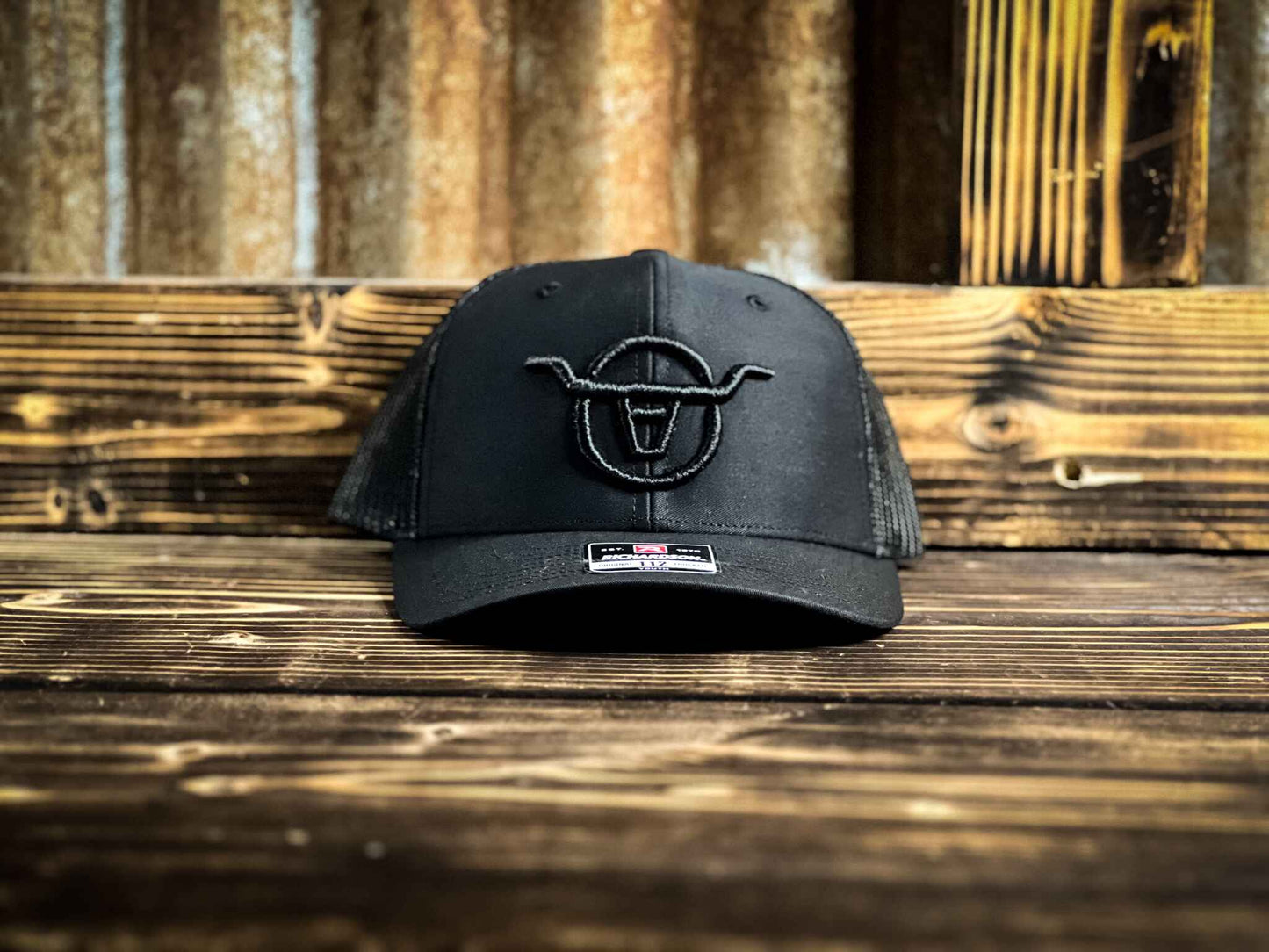 Youth size black mesh back trucker hat with Angels and Outlaws Co bull logo embroidered on the front with black thread