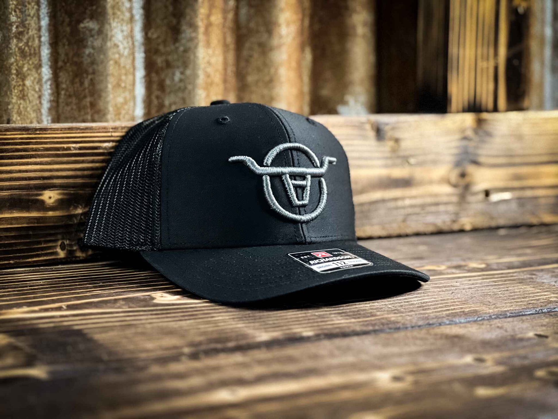 Youth size black mesh back trucker hat with Angels and Outlaws Co bull logo embroidered on the front with grey thread