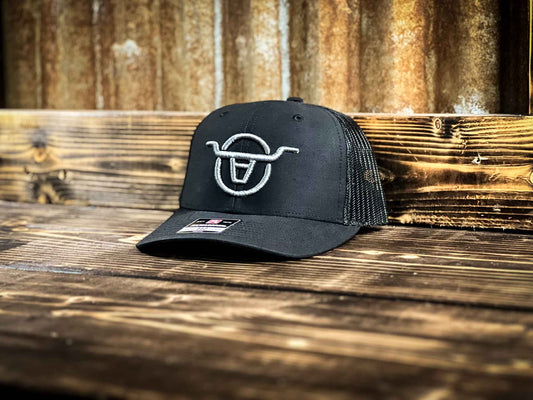 Youth size black mesh back trucker hat with Angels and Outlaws Co bull logo embroidered on the front with grey thread