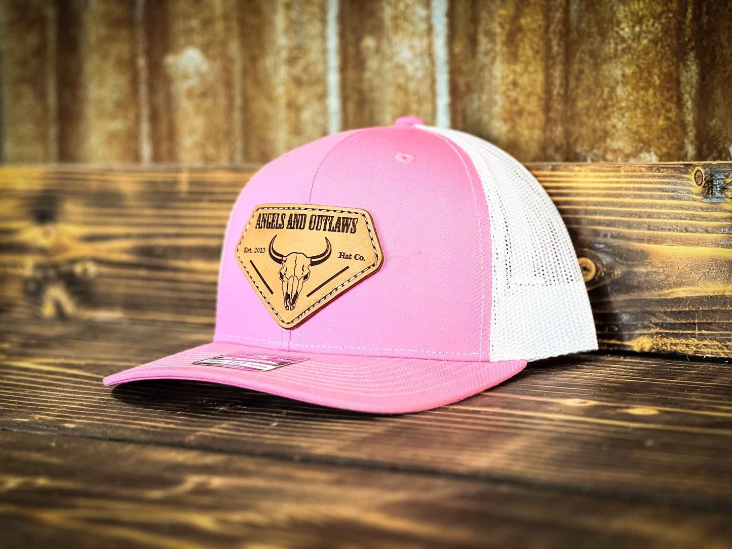 Pink front white back Mesh back trucker hat with Angels and Outlaws name and a bison skull engraved on a leather patch