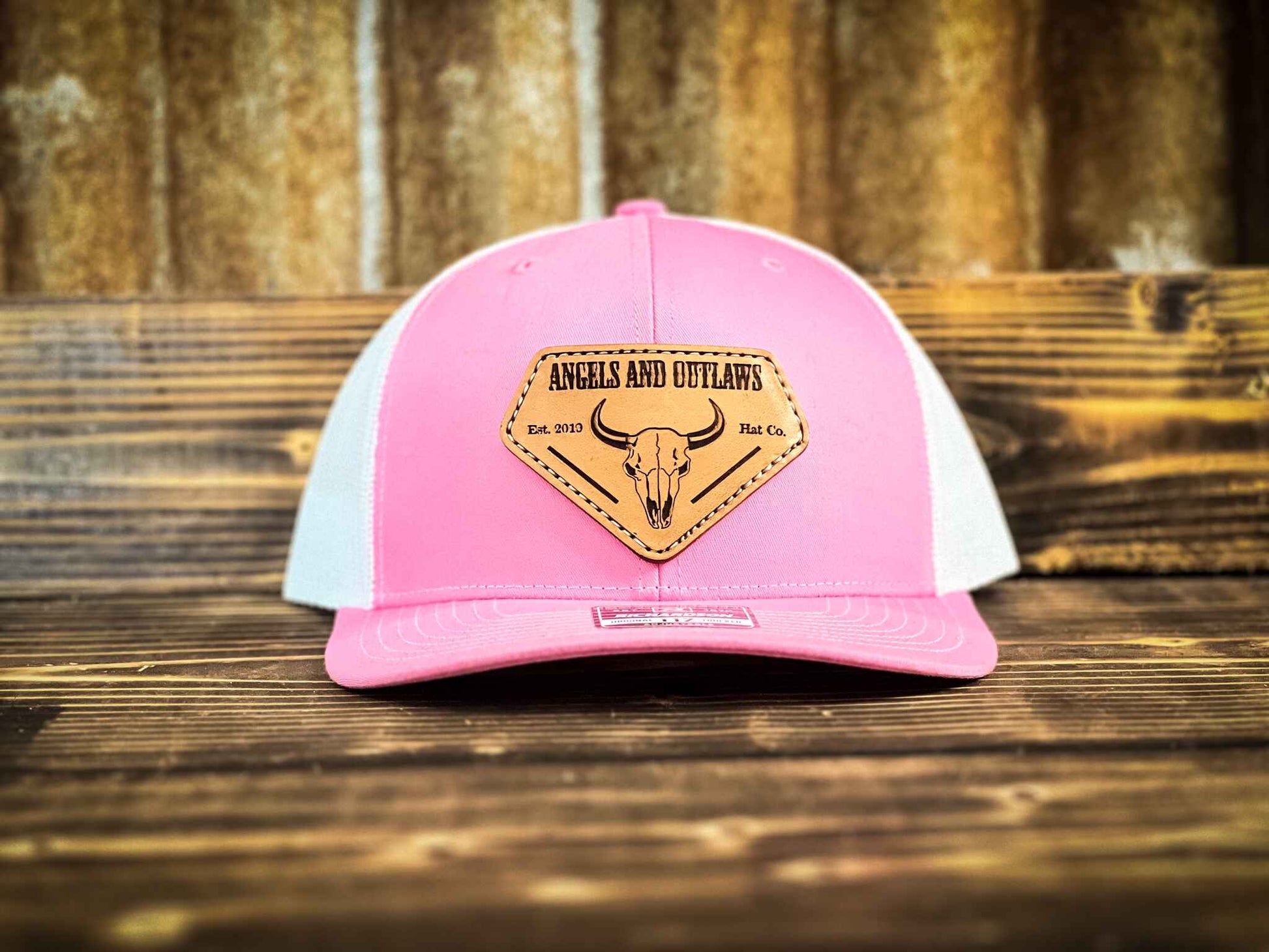 Pink Front white back Mesh back trucker hat with Angels and Outlaws name and a bison skull engraved on a leather patch