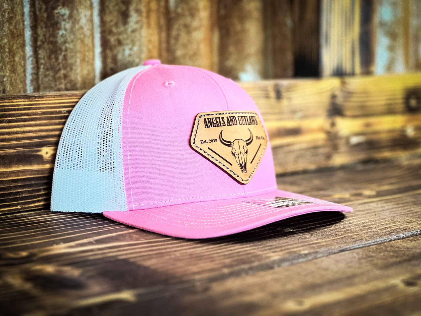 Pink front white back Mesh back trucker hat with Angels and Outlaws name and a bison skull engraved on a leather patch