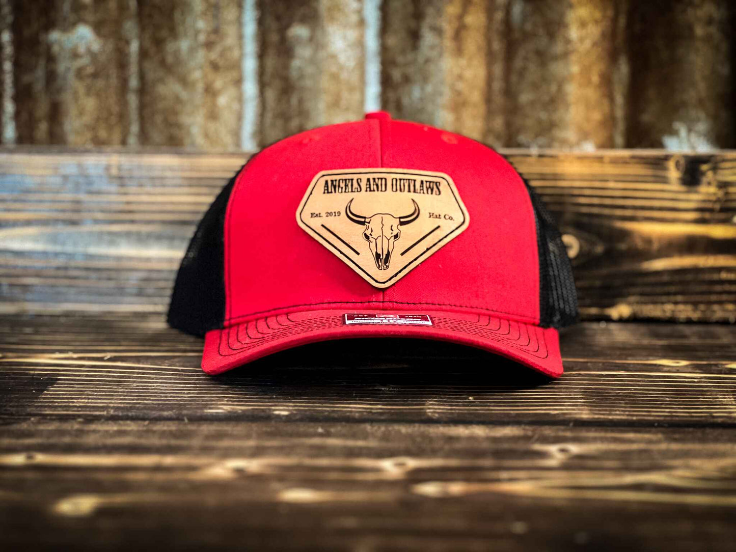 Red front black back mesh back trucker hat with Angels and Outlaws name and a bison skull engraved on a leather patch