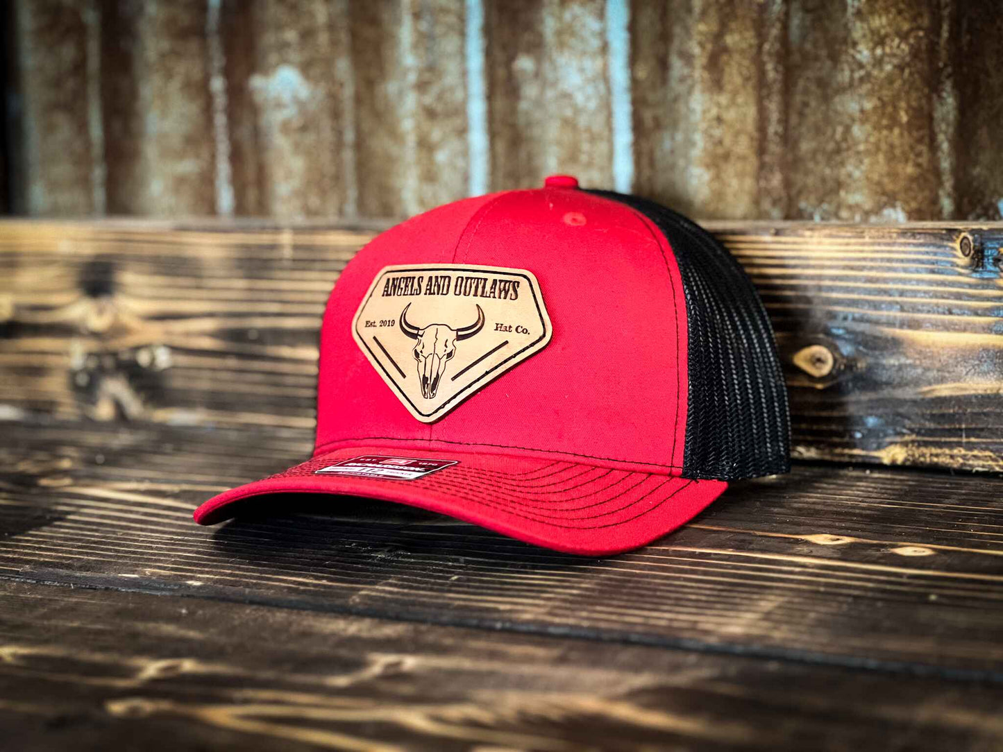 Red front black back Mesh back trucker hat with Angels and Outlaws name and a bison skull engraved on a leather patch
