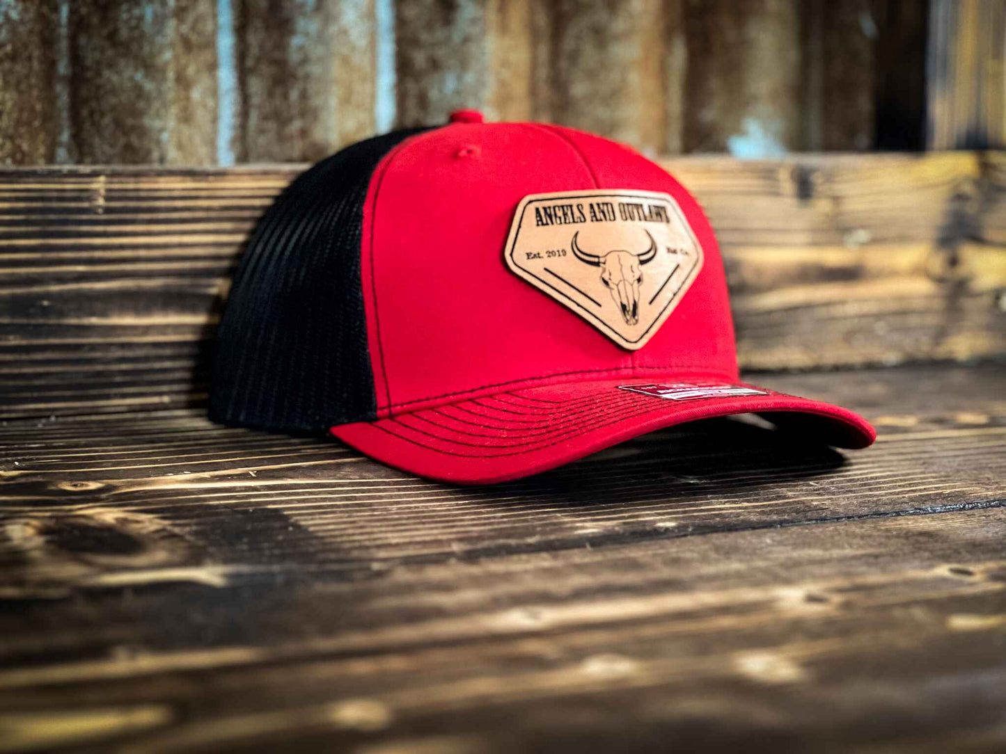 Red front black back mesh back trucker hat with Angels and Outlaws name and a bison skull engraved on a leather patch